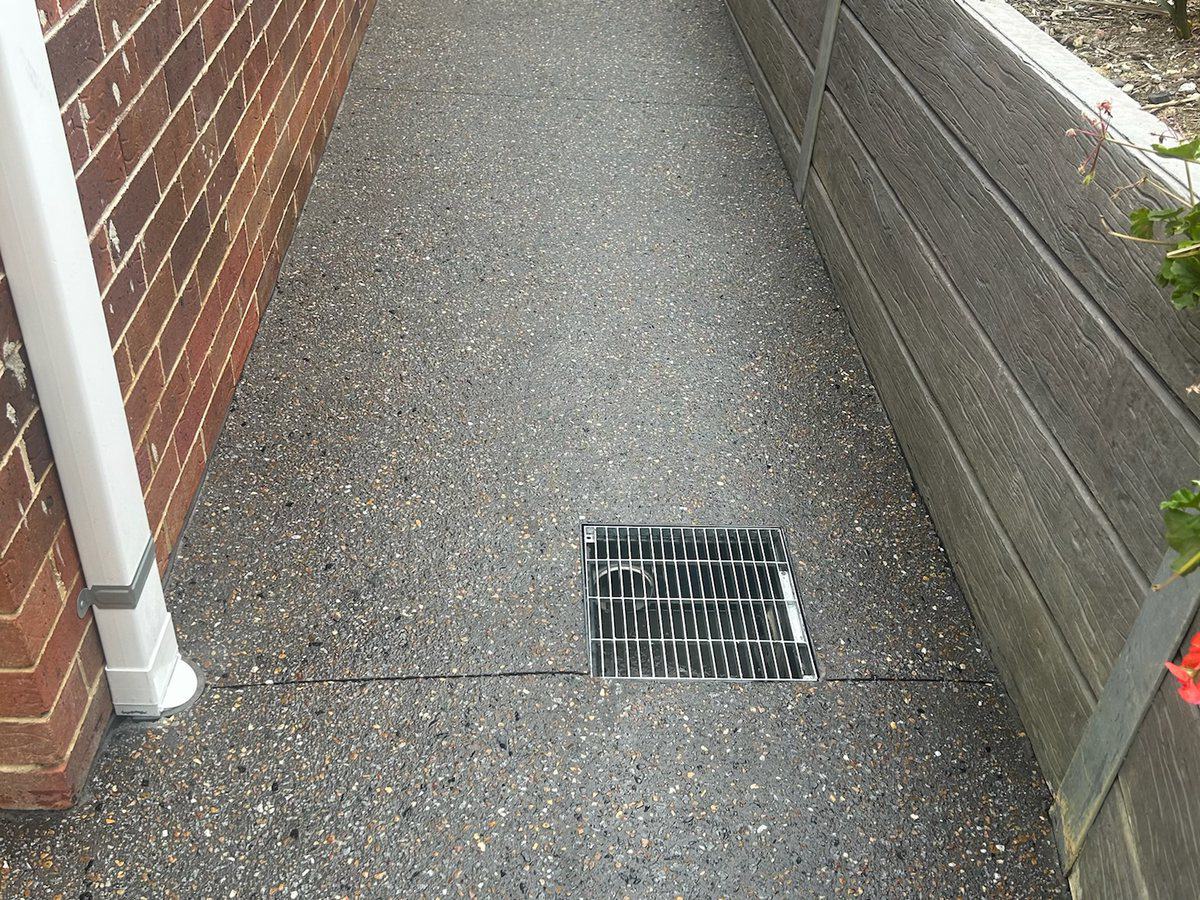 Exposed aggregate path with a drainage grate set flush into the slab