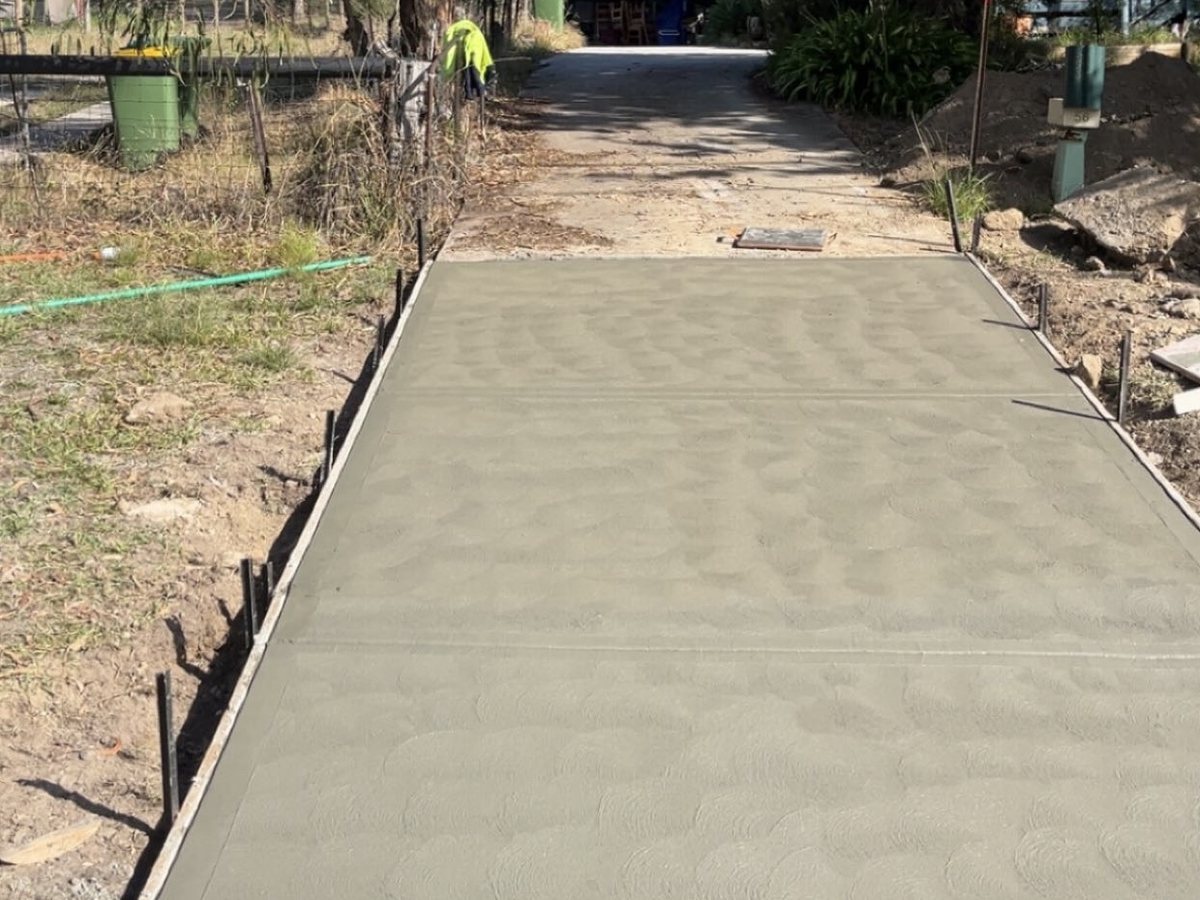 Plain concrete driveway freshly poured and floated, running to the rear of a property