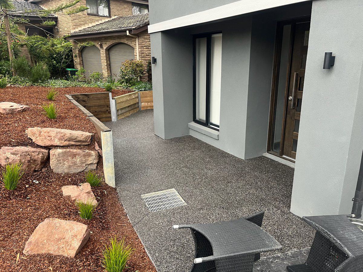 Charcoal exposed aggregate entrance landing wrapping around to the front door, beside landscaped beds