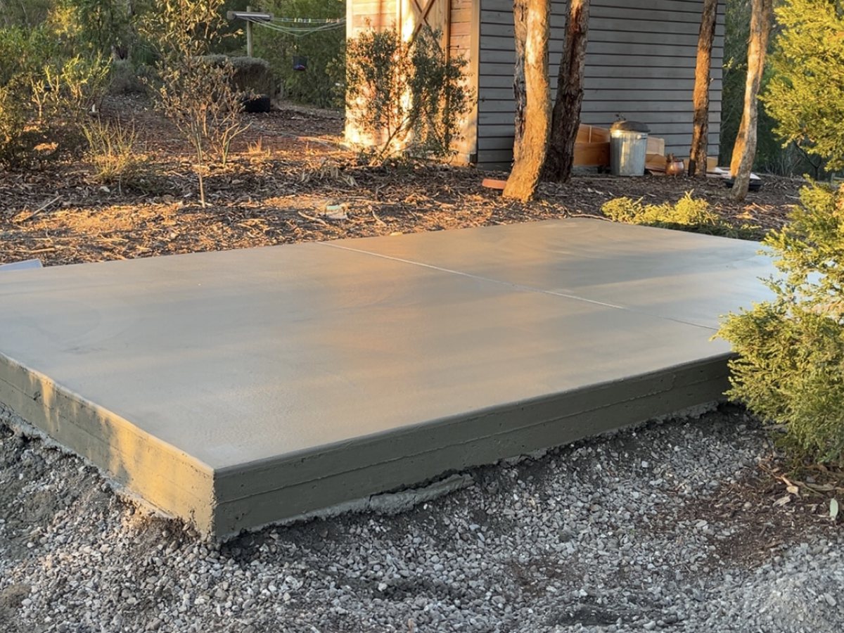 Shed slab poured and edged on a compacted gravel pad beside an existing shed