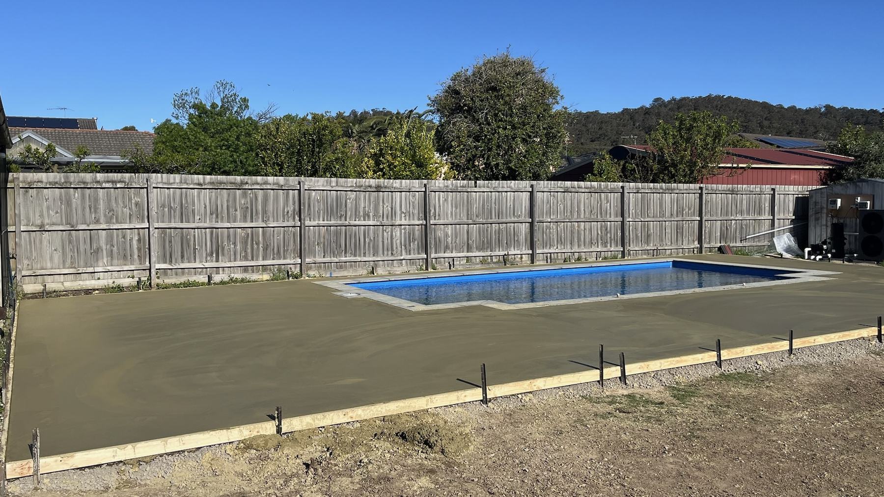 Freshly poured concrete pool surround running up to the pool coping