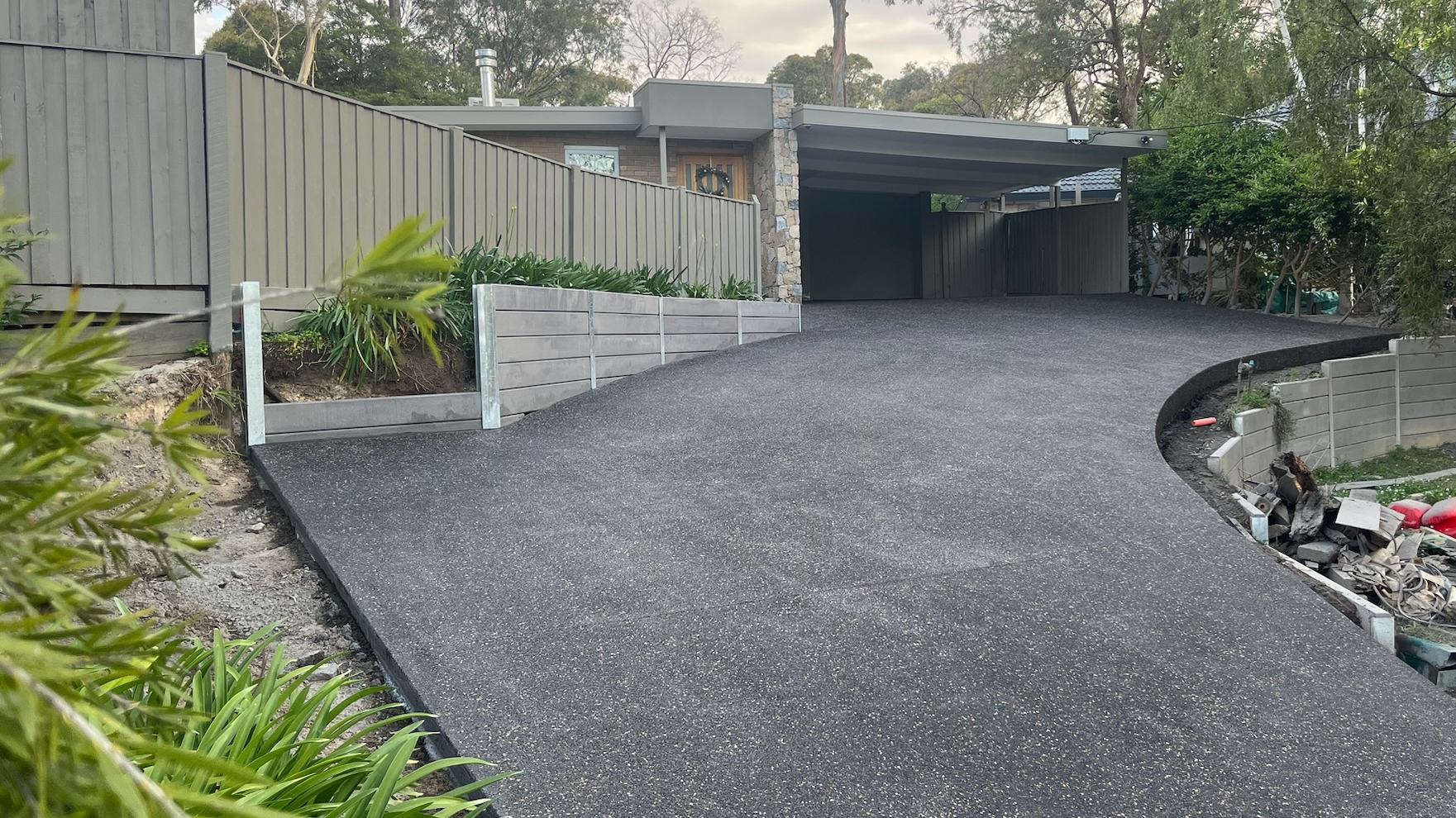 Charcoal exposed aggregate driveway curving up to a carport, framed by gum trees in Melbourne's eastern suburbs